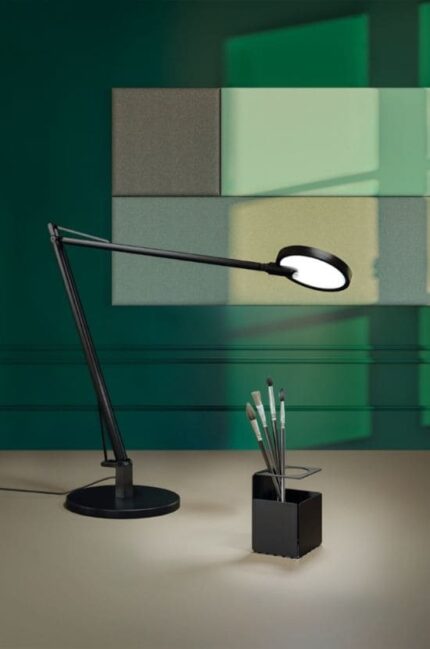 Lampe de bureau noire au design moderne avec bras articulé, posée devant un fond vert élégant, accompagnée d’un porte-stylos minimaliste