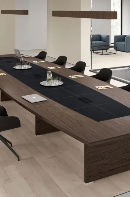 Conçue pour les grandes tables modulaires, la collection Odeon se distingue dans sa version bois, où un insert en cuir avec coutures contrastantes apporte un charme unique.