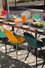 Chaises aux couleurs éclatantes, fabriquées à partir de matériaux recyclés, disposées autour d'une table en bois pour un repas convivial en extérieur.