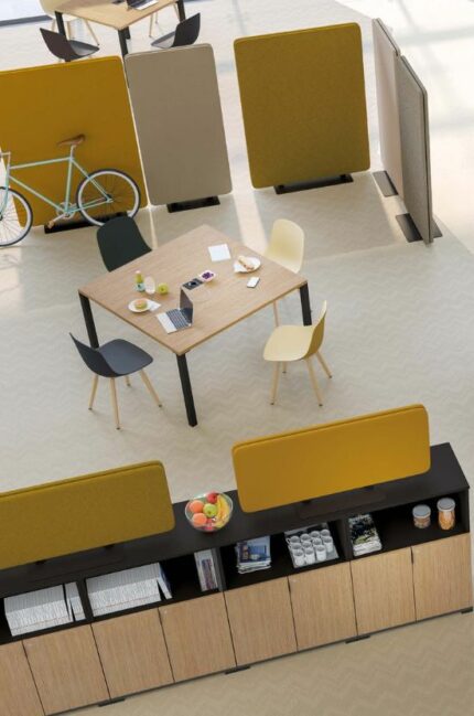 Espace de coworking équipé de cloisons acoustiques Taoma jaunes et beiges, avec des tables de réunion modernes et une étagère en bois noir pour un aménagement fonctionnel et convivial.